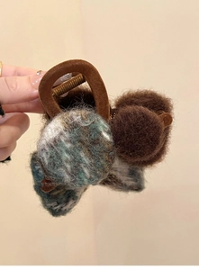 Detail of plush brown pompom and mixed green knit texture on hair claw clip