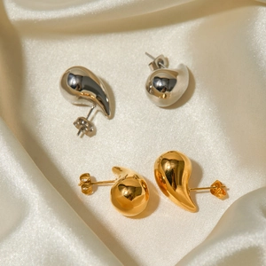 Detailed view of teardrop earrings in polished gold and silver on silk fabric