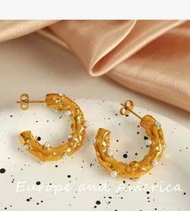 Detailed shot of gold-plated C-shape earrings with rhinestones and pearls on silk
