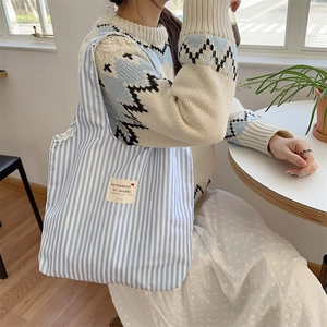 Detail of blue striped canvas tote bag with woven label on model in bright indoor setting