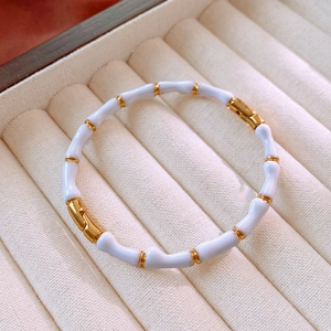 Dettaglio di bracciale a bambù in smalto crema e oro con chiusura su vassoio velluto
