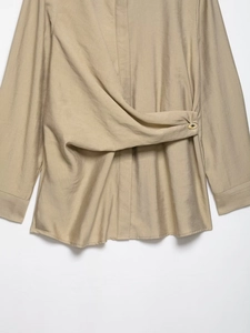 Detail view of khaki shirt with crossover waist pleated design and gold button accent
