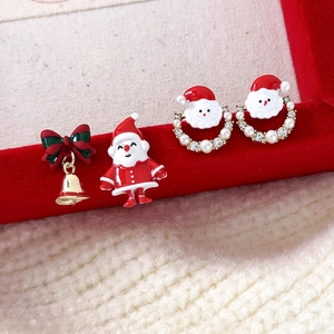Macro view of asymmetric Santa Claus and Christmas bell earrings on red velvet cloth