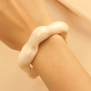 Close-up of a chunky cream white wavy resin open cuff bracelet worn on a wrist