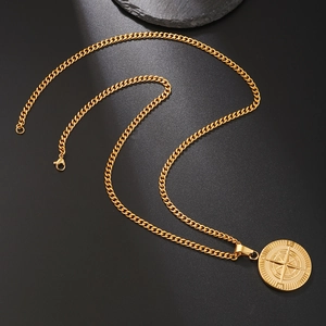 Detail shot of golden compass pendant on cuban chain against black background