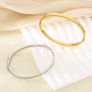 Detail of minimalist gold and silver oval bangles on a luxury silk and stone background
