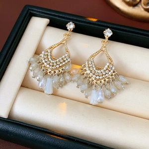Detail of bohemian gold drop earrings with white beads on a beige jewelry cushion