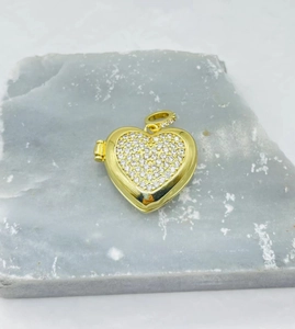 Detail of a golden heart locket pendant with crystal pavé on a textured stone surface