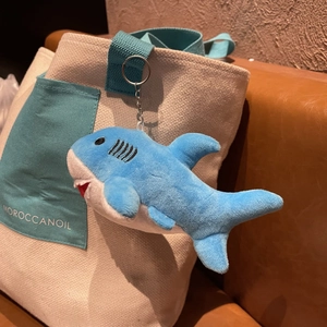 Cute blue shark plush keychain made of soft fabric hanging on a beige canvas bag