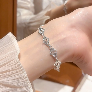 Close-up of silver hollow clover bracelet worn on wrist with white pleated cuff sleeve