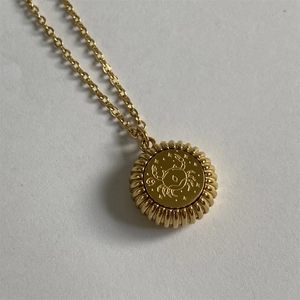 Close-up of gold Cancer zodiac coin pendant with embossed details on a fine chain