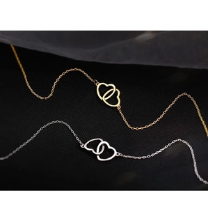 Close-up of interlocking heart pendants in gold and silver finishes on black fabric