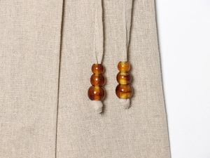 Detail of linen drawstring waist with triple amber resin beads on a beige summer outfit