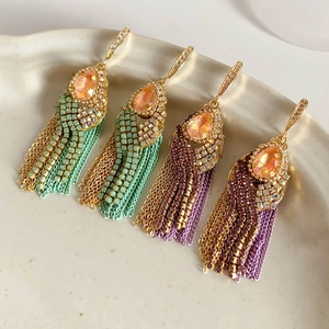 Detail of bohemian gold earrings with orange teardrop stones and colorful beaded tassels