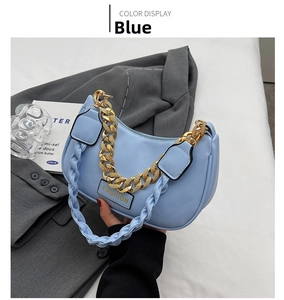 Detail of light blue crescent bag with chunky gold chain and woven strap on white fabric