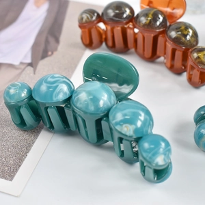 Detail of dark green and amber marble-patterned shark hair clips with pearl top accents