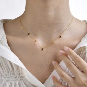 Detailed view of women's gold chain necklace with black rectangle charms on the collarbone