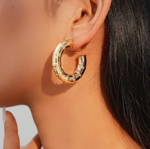 Close-up of chunky gold hoop earring with bamboo texture on female model ear