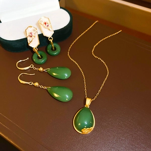Detailed set of gold plated jewelry with green teardrop glass and zircon on leather background