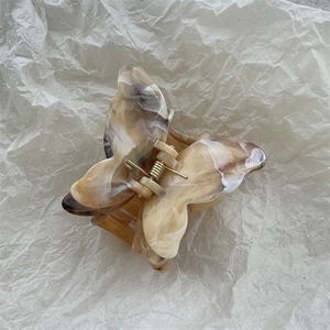 Macro detail of butterfly hair claw with marble texture and golden metal spring