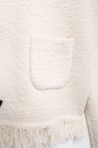 Detail shot of the cream-white textured knit cardigan featuring fringe hem and side pocket