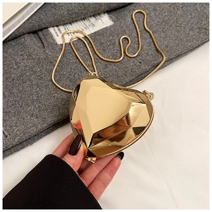 Detail of a mini gold heart-shaped crossbody bag with a faceted geometric surface and chain