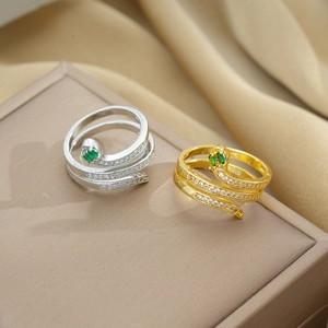 Close-up of gold and silver snake rings with green emerald eyes and crystal details