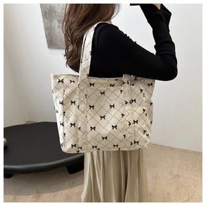 Detailed view of beige tote bag with black bow patterns and diamond quilt texture
