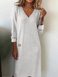 Detail of light grey V-neck knit dress featuring a small brown square leather waist tag