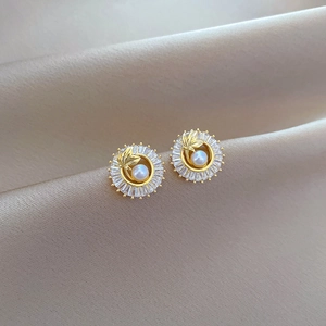 Primer plano de aretes de titanio con perlas y circonitas brillantes sobre seda champán
