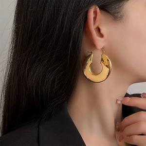 Macro side view of large polished gold U-shape chunky earrings worn by model