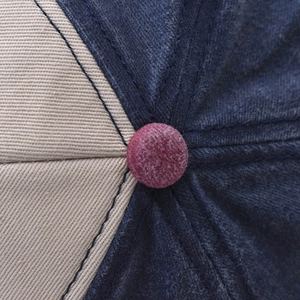Detail of a navy and beige baseball cap with a burgundy suede top button and stitched seams