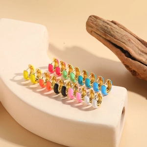 Detail of colorful enamel hoop earrings in gold finish set on a minimalist display stand