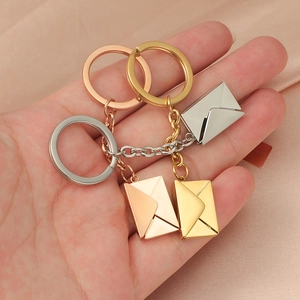 Three-piece metal envelope keychains in gold silver and rose gold held against silk fabric