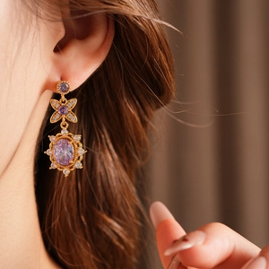 Detail of vintage gold flower earring with purple gemstone and zircon worn by a model
