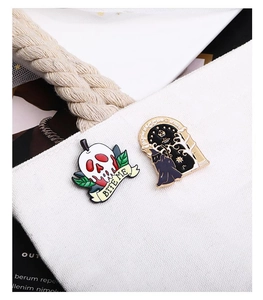Detail of gothic enamel pins with skull and starry night designs on a white canvas bag