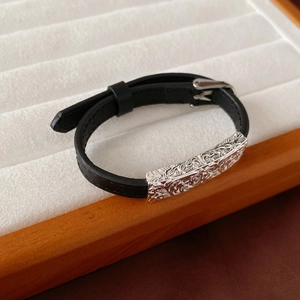 Close-up of black leather bracelet with an intricately engraved silver metal buckle detail