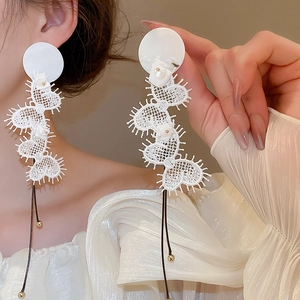 Detail of white heart-shaped lace drop earrings with pearl studs and black tassels on model