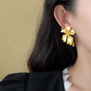 Close-up of a large matte gold floral earring on a model for a vintage French look