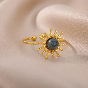 Macro shot of gold sun-shaped ring with dark stone inlay on elegant champagne satin