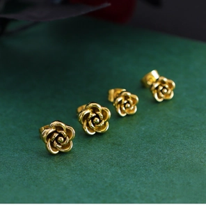 Macro shot of 3D rose flower earrings in vintage gold finish on a dark green background
