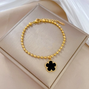 Detail of gold beaded bracelet with black clover pendant and lobster clasp on white silk