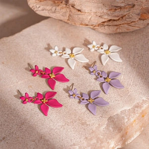 Trois paires de boucles d'oreilles fleuries en blanc, magenta et violet sur pierre