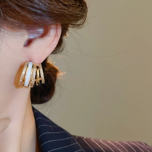 Detail of layered gold-plated C-shaped earrings with zircons worn by a model