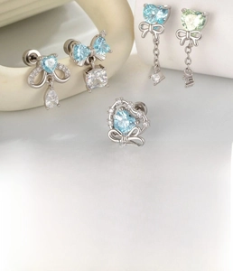 Detailed view of silver bow and heart stud earrings with blue zircon on white ceramic