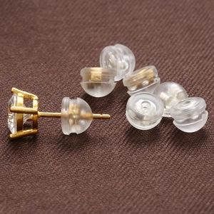 Macro view of gold-plated stud earring with clear gemstone and silicone backs