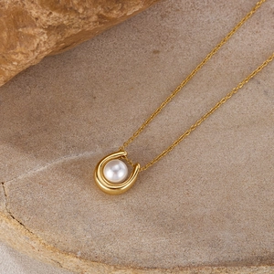 Detail of a U-shaped gold pendant necklace with a white pearl on a natural rock background