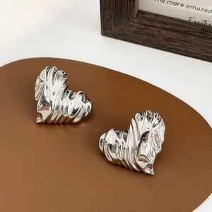Detail view of silver heart earrings with textured metallic pleats on leather background