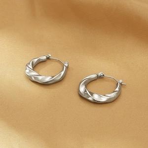Macro shot of silver twisted stainless steel hoop earrings on gold silk fabric