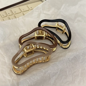 Three acetate hair claw clips in black, brown, and beige with gold metal base details